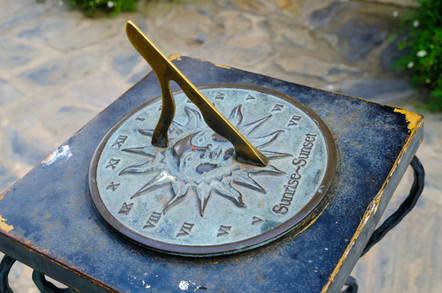 Close-up of a brass sundial mounted on a stone plinth in a garden