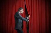 Curious actor or illusionist is looking behind red curtain