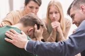 Devastated young man and friends supporting him during group therapy