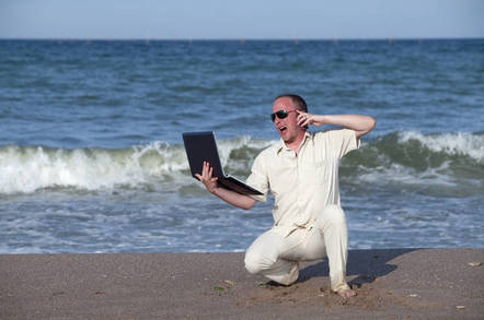 sunburned man shouts down phone while on laptop on the beach