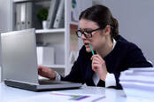 Someone chewing nervously on a pencil at work in front of a laptop