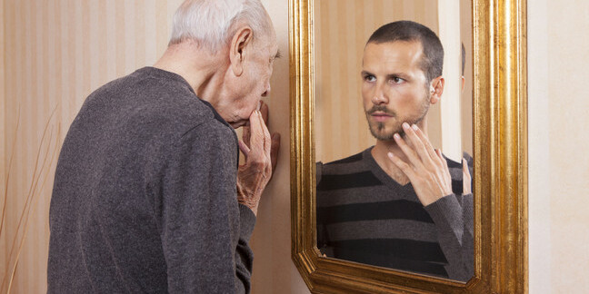 Older man looking at younger self in the mirror