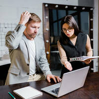 Someone pointing out an error on a colleague's laptop