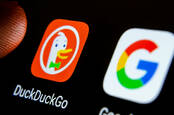 DuckDuckGo app on a smartphone screen next to Google search app and a finger touching it. Selective focus.