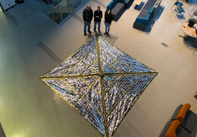 Drone view of the Spinnaker3 drag sail prototype, fully deploying in the atrium of the Neil Armstrong Hall of Engineering at Purdue University. Pictured from left to right: Anthony Cofer, David Spencer, Arly Black