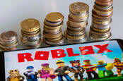 Roblox on a mobile phone, beside piles of coins