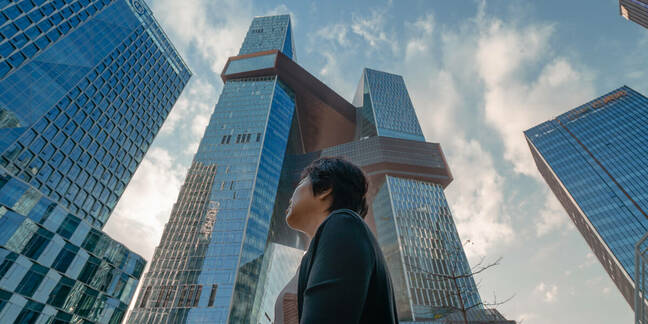 A woman looks at the sky while walking through the streets of Shenzhen against the backdrop of the Tencent Building