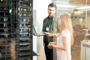 Two people standing next to racks of servers discussing work