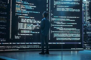 Someone standing in front of giant screens of software source code