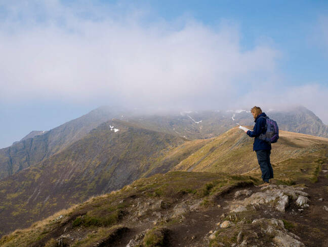 Un caminante solitario mira un mapa en el camino hacia la brumosa cumbre de Blencathra (también conocida como Saddleback) en el Lake District, Cumbria, Reino Unido, con una nube cayendo contra un cielo azul